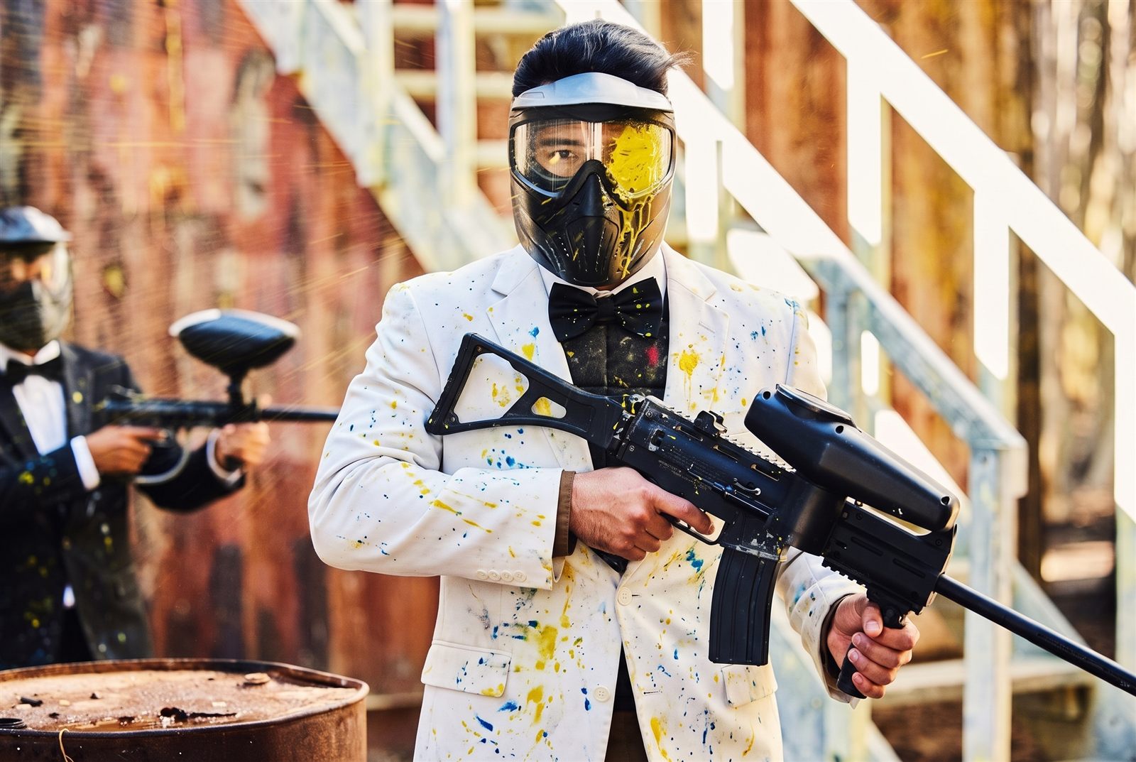 Groom in a paint-splattered white suit and bow tie holding a paintball marker